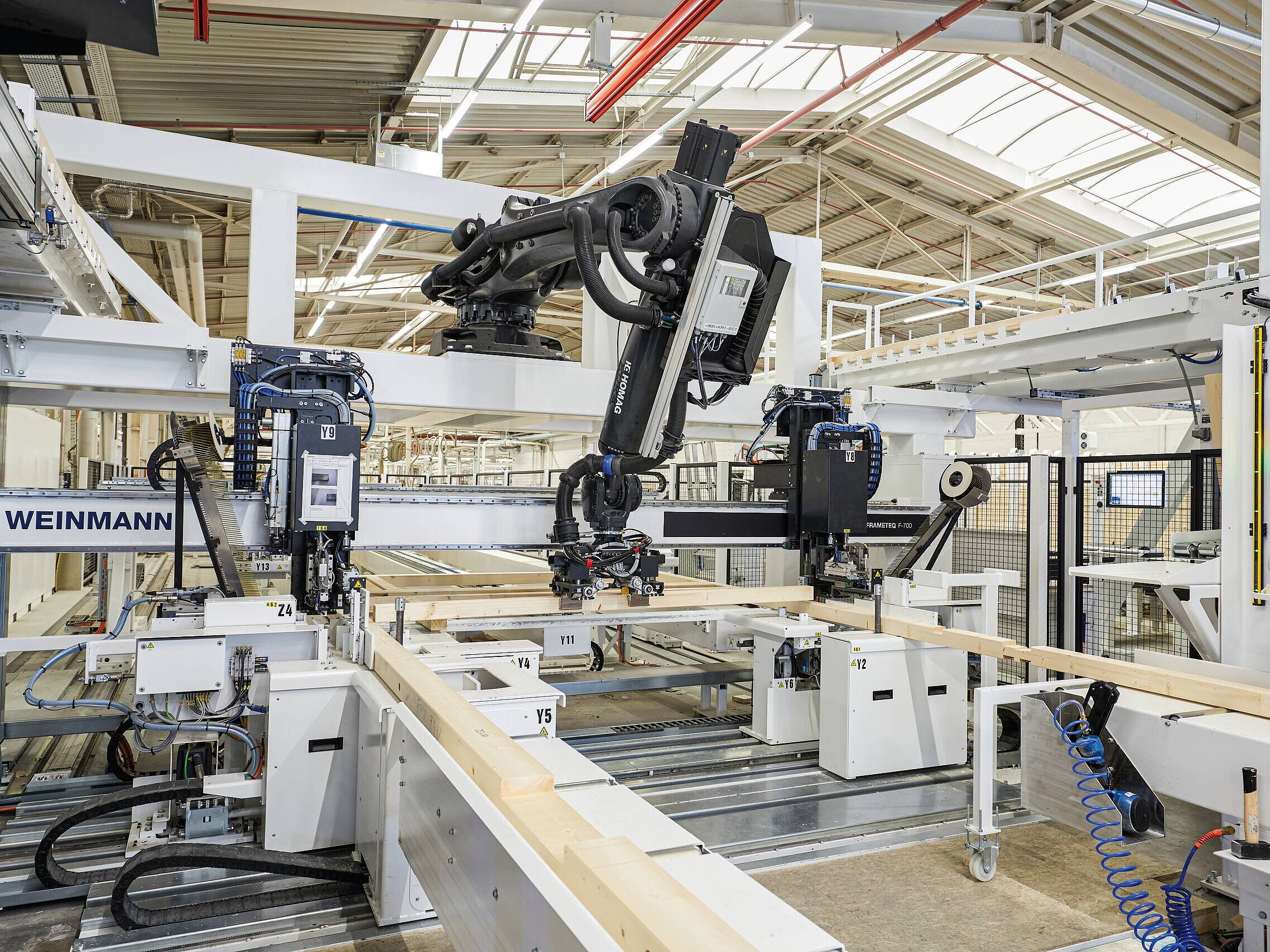 Eine moderne automatisierte Maschinenlinie in einer Produktionshalle, die Holzlatten bearbeitet. Roboterarme und Maschinen sind sichtbar, die präzise Arbeiten an den Holzstücken durchführen. Die Umgebung ist hell erleuchtet und technisch ausgestattet.